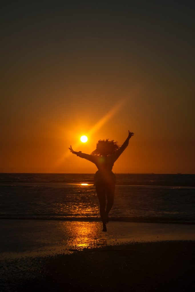 silhouette of woman standing on beach during sunset